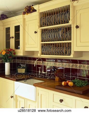 Stock Photo - Fitted wooden plate rack above underset Belfast sink in cream kitchen. Fotosearch