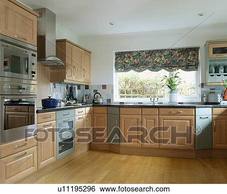 Stock Photograph - Fitted wooden units and wooden flooring in modern kitchen with floral blind on window. Fotosearch