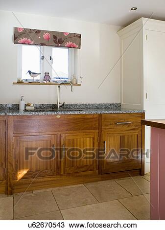 Stock Image - Floral blind on small window above sink in modern country kitchen with dark wood fitted units. Fotosearch
