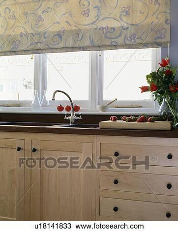 Stock Image - Floral blind on window above sink and chrome tap in fitted unit. Fotosearch