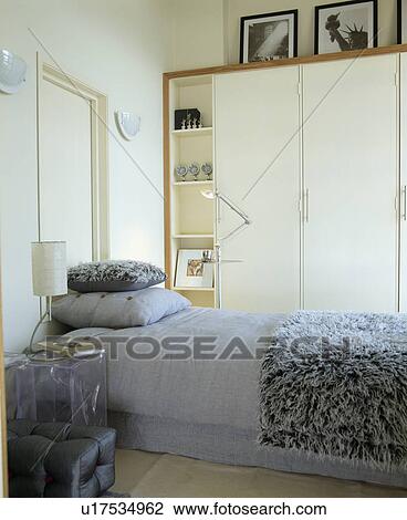 Fluffy grey throw and grey bedlinen on bed in modern bedroom with cream fitted wardrobe View Large Photo Image Stock Image - Fluffy grey throw and grey bedlinen on bed in modern bedroom with cream fitted wardrobe. Fotosearch
