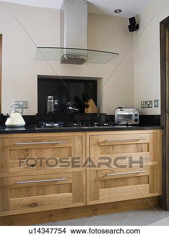 Glass and steel extractor above hob in fitted oak unit in modern kitchen with chrome toaster on worktop View Large Photo Image Picture - Glass and steel extractor above hob in fitted oak unit in modern kitchen with chrome toaster on worktop. Fotosearch