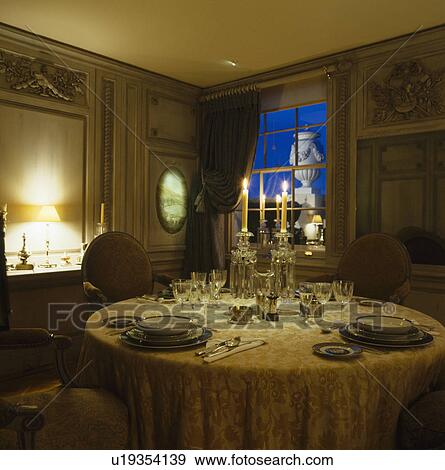 Stock Photo - Glass candelabra on table with silk cloth set for dinner in panelled candlelit dining room. Fotosearch