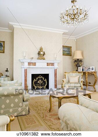 Stock Image - Glass chandelier and gilt furniture in neutral country living room. Fotosearch