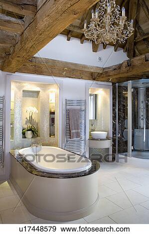 Glass chandelier on wooden beamed ceiling above bath in modern bathroom View Large Photo Image Stock Photo - Glass chandelier on wooden beamed ceiling above bath in modern bathroom. Fotosearch