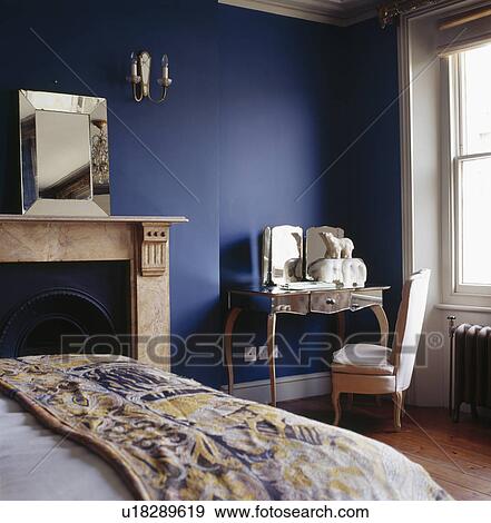Glass-framed mirror above marble fireplace in blue bedroom with patterned throw on the bed View Large Photo Image Stock Photo - Glass-framed mirror above marble fireplace in blue bedroom with patterned throw on the bed. Fotosearch