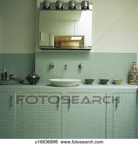 Stock Photograph - Glass-fronted cabinet above basin in pastel blue mosaic-tiled modern vanity unit. Fotosearch