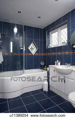 Glass shower doors on curved white bath in black tiled bathroom View Large Photo Image Picture - Glass shower doors on curved white bath in black tiled bathroom. Fotosearch