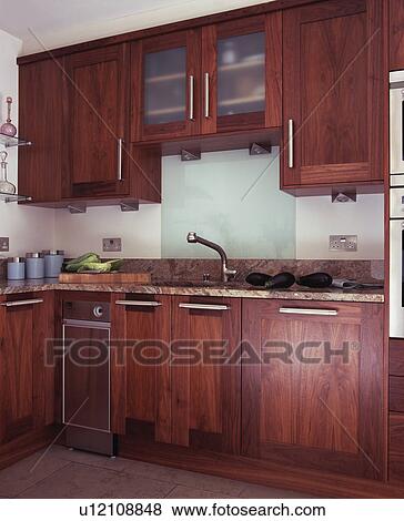 Stock Photo - Glass splashback above sink in modern kitchen with dark wood fitted units. Fotosearch