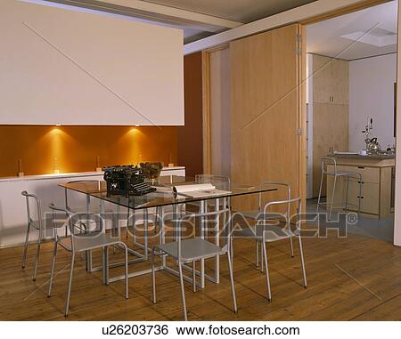 Stock Photograph - Glass table and metal chairs in dining room with orange wall and wooden flooring. Fotosearch