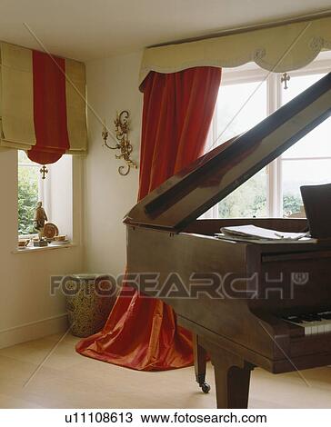 Stock Image - Grand piano in living room with striped blind and red silk curtains. Fotosearch