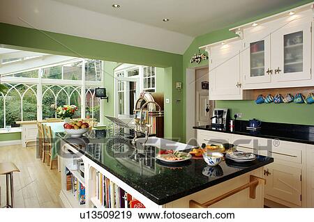 Granite-topped island unit in large green kitchen with conservatory dining room extension View Large Photo Image Stock Photo - Granite-topped island unit in large green kitchen with conservatory dining room extension. Fotosearch