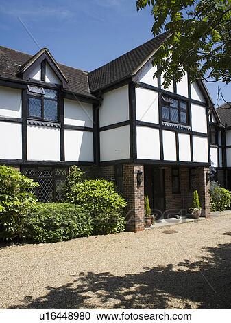 Stock Image - Gravel drive in front of black+white traditional house. Fotosearch