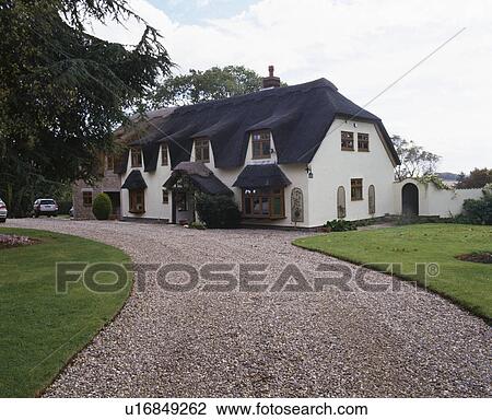 Stock Image - Gravel drive to thatched country house. Fotosearch