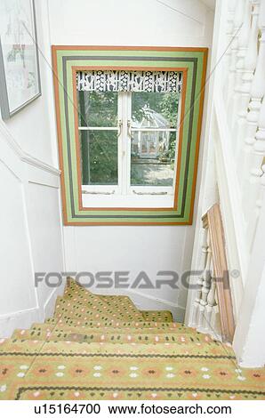 Stock Image - Green and red painted border around window above staircase with yellow and green patterned carpet. Fotosearch