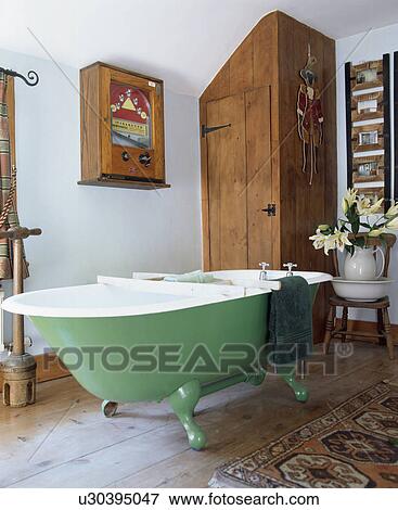 Stock Photo - Green clawfoot bath in pastel blue bathroom with fitted wooden cupboard. Fotosearch