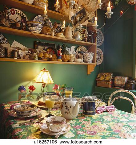 Green dining room with lighted lamp and old teaset on table with green floral cloth below shelves with collection of pottery View Large Photo Image Stock Photograph - Green dining room with lighted lamp and old teaset on table with green floral cloth below shelves with collection of pottery. Fotosearch