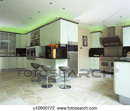 Stock Image - Green halogen lighting above fitted cupboards in modern kitchen with limestone floor and fitted white units. Fotosearch