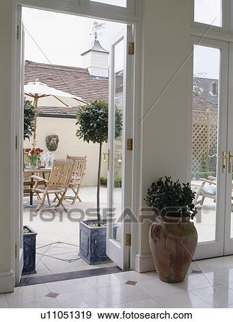 Stock Photo - Green houseplant in terracotta pot beside open glass doors to patio. Fotosearch