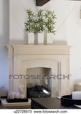 Stock Image - Green leaves in three white vases on stone fireplace. Fotosearch