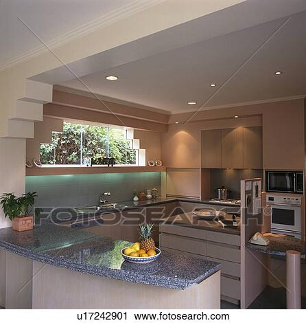 Stock Image - Grey granite worktop on peninsular unit in modern pink kitchen. Fotosearch