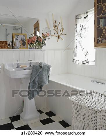 Stock Image - Grey towel on white pedestal basin in white cottage bathroomn with white wicker linen basket. Fotosearch