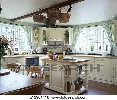 Stock Photograph - Island unit in traditional cream country kitchen with baskets on wooden ceiling beam. Fotosearch