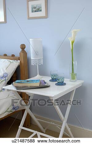 Lamp and books on small white painted bedside table in pastel blue bedroom View Large Photo Image Stock Photo - Lamp and books on small white painted bedside table in pastel blue bedroom. Fotosearch