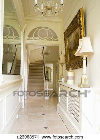 Stock Image - Lamp on radiator cover in narrow cream hall with view of staircase. Fotosearch