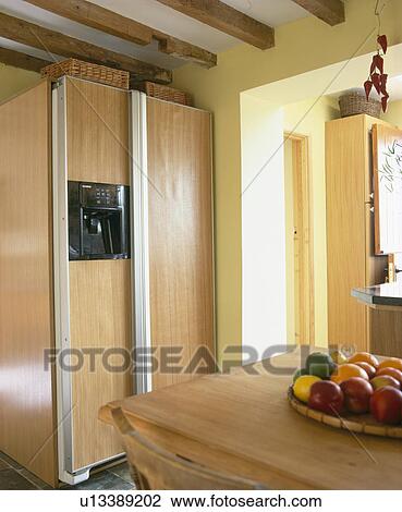 Stock Image - Large American-style fridge-freezer concealed behind wooden doors. Fotosearch