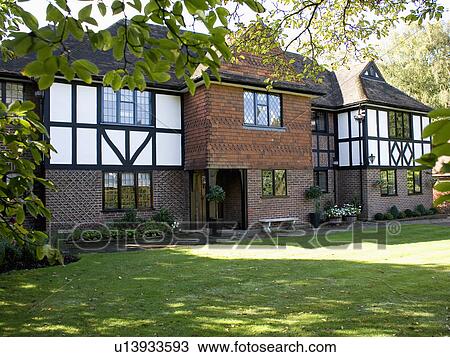Stock Image - Large black+white timbered and brick house in the country with shady lawn. Fotosearch