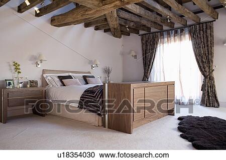 Large cabinet with concealed television below bed in modern bedroom with beamed ceiling View Large Photo Image Stock Image - Large cabinet with concealed television below bed in modern bedroom with beamed ceiling. Fotosearch