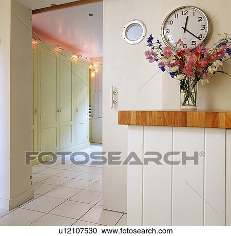 Stock Image - Large circular clock on wall beside sliding door to bedroom with fairy lights above pale green fitted wardrobe. Fotosearch