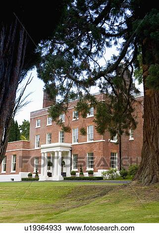 Stock Image - Large conifer tree on lawn in front of Georgian country house. Fotosearch