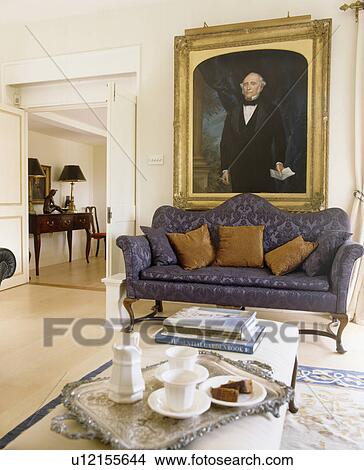 Large gilt-framed oil portrait above blue sofa in townhouse living room with coffee-pot and cups on silver tray on stool View Large Photo Image Picture - Large gilt-framed oil portrait above blue sofa in townhouse living room with coffee-pot and cups on silver tray on stool. Fotosearch