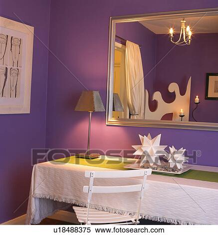 Large gilt mirror on wall of purple dining room with lighted lamp and white cloth on rectangular table View Large Photo Image Stock Photography - Large gilt mirror on wall of purple dining room with lighted lamp and white cloth on rectangular table. Fotosearch