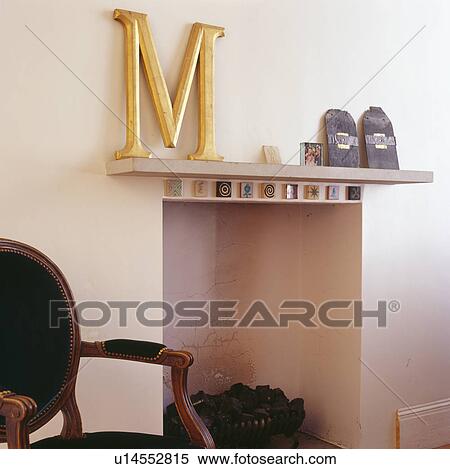 Stock Photography - Large gold letter M on mantelpiece above modern fireplace. Fotosearch