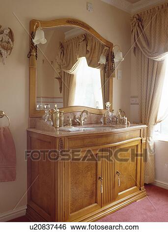 Stock Photograph - Large mirror above pale wood vanity unit. Fotosearch
