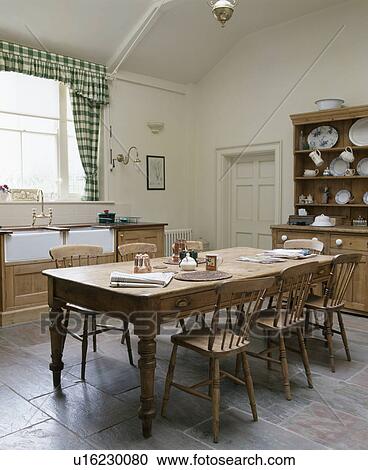 Stock Image - Large old wooden table and chiars in country kitchen with flagstone floor and pine dresser. Fotosearch