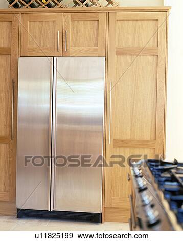 Stock Photo - Large stainless steel American-style fridge-freezer in pale wood fitted unit. Fotosearch