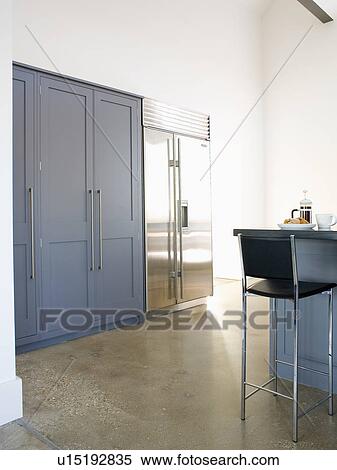 Stock Photography - Large stainless-steel American-style fridge freezer in modern kitchen with concrete flooring. Fotosearch
