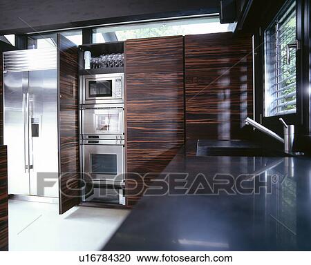 Stock Image - Large stainless steel fridge freezer in modern kitchen with sink in black granite worktop. Fotosearch