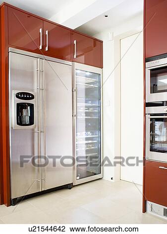 Stock Image - Large stainless-steel fridge freezer with tall wine-cooler in red fitted unit in modern kitchen. Fotosearch