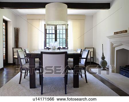 Stock Photograph - Large white ceiling light in monochromatic country dining room with black chairs upholstered in white on white rug. Fotosearch