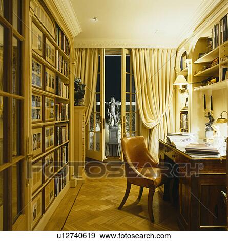 Stock Photo - Leather chair and antique desk in study with parquet floor and cream curtains at French doors. Fotosearch