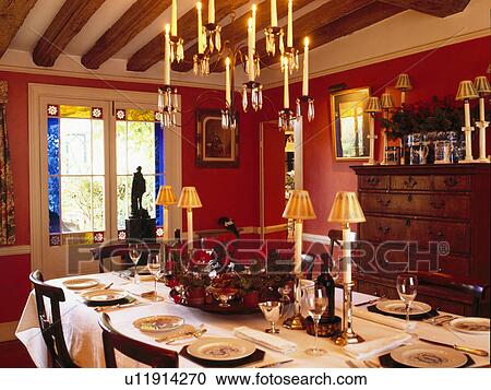 Stock Image - Lighted candelabra above table set for lunch in pink cottage dining room. Fotosearch
