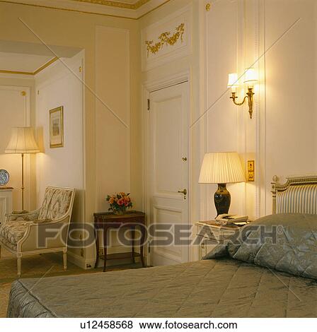 Lighted lamp and wall-light in traditional cream townhouse bedroom View Large Photo Image Stock Photo - Lighted lamp and wall-light in traditional cream townhouse bedroom. Fotosearch