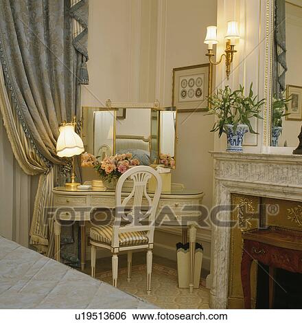 Stock Photograph - Lighted lamp on dressing-table with triple mirror in townhouse bedroom. Fotosearch