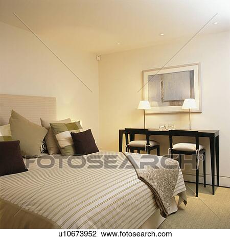 Stock Image - Lighted lamps and neutral bedlinen in townhouse bedroom. Fotosearch
