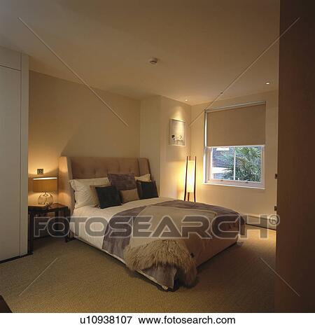 Stock Photo - Lighted lamps and neutral bedlinen in townhouse bedroom with cream blind. Fotosearch